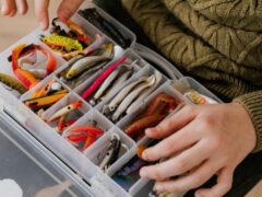 Close-up of assorted fishing lures neatly arranged in a plastic tackle box held by a person., tags: salt pencil der für - pexel