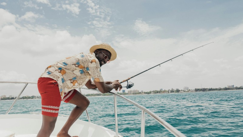Smiling man fishing on a yacht in sunny weather, enjoying leisure in vibrant tropical waters., tags: moderne kurze - pexel