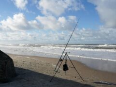 A lone fishing rod stands on a remote beach in Søndervig, Denmark against a backdrop of breaking waves and a vast horizon., tags: für - pexel